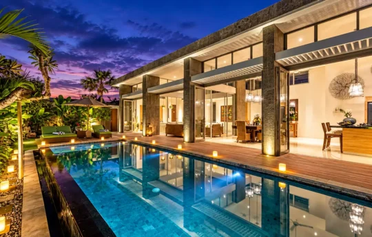 Villa Bamboo swimming pool and sunbeds with view of interiors at night with lights on